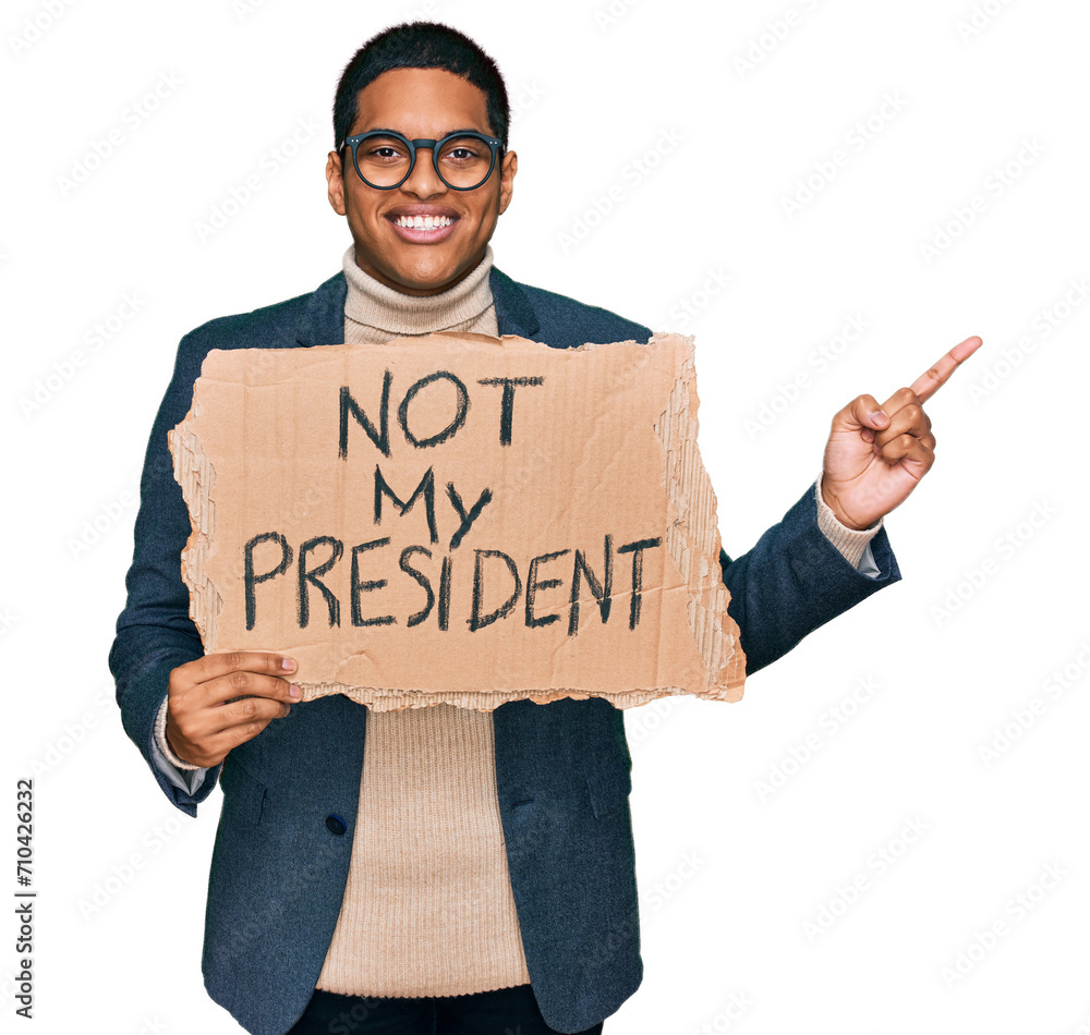 Young handsome hispanic man holding not my president protest banner smiling happy pointing with hand and finger to the side Young handsome hispanic man holding not my president protest banner smiling happy pointing with hand and finger to the side