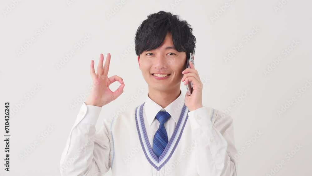 スマートフォンで電話をしながらOKサインをする男子高校生 白背景 スマートフォンで電話をしながらOKサインをする男子高校生 白背景
