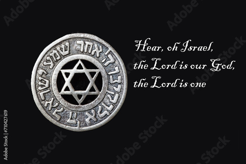 Silver medallion with the Star of David and the Shema Israel prayer in Hebrew. On a black background, the text of the prayer is in English.