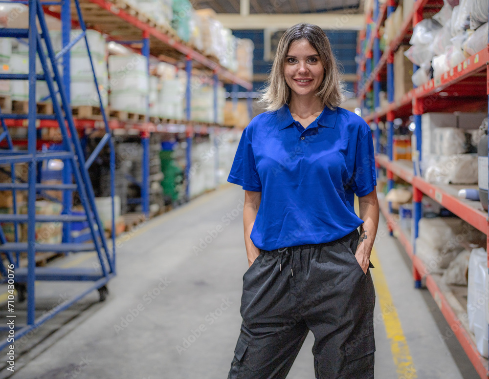 Fototapeta premium Confident female warehouse worker standing in logistic storage looking at camera smiling. Young adult manager employee working in merchandise distribution storehouse. Inventory order service staff.