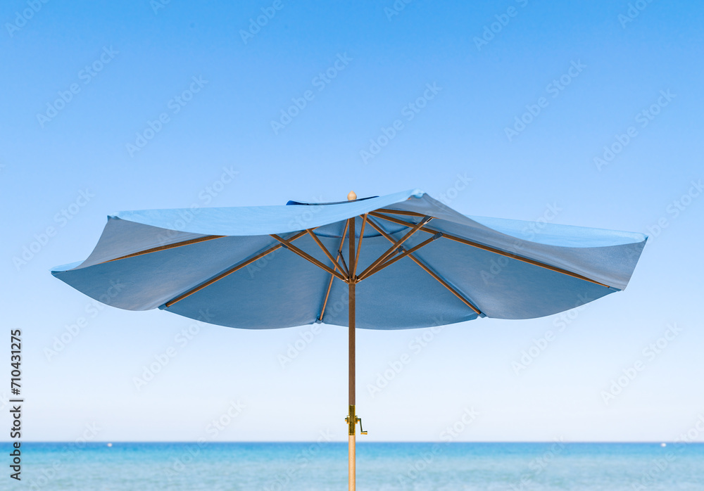 close-up view of a blue beach umbrella with its structure contrasted against a clear sky and tranquil ocean backdrop. Summer vacation concept