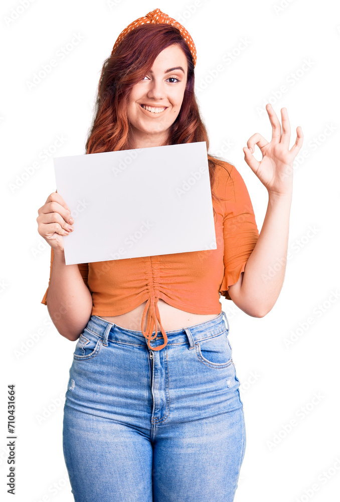 Young beautiful woman holding cardboard banner with blank space doing ok sign with fingers, smiling friendly gesturing excellent symbol Young beautiful woman holding cardboard banner with blank space doing ok sign with fingers, smiling friendly gesturing excellent symbol