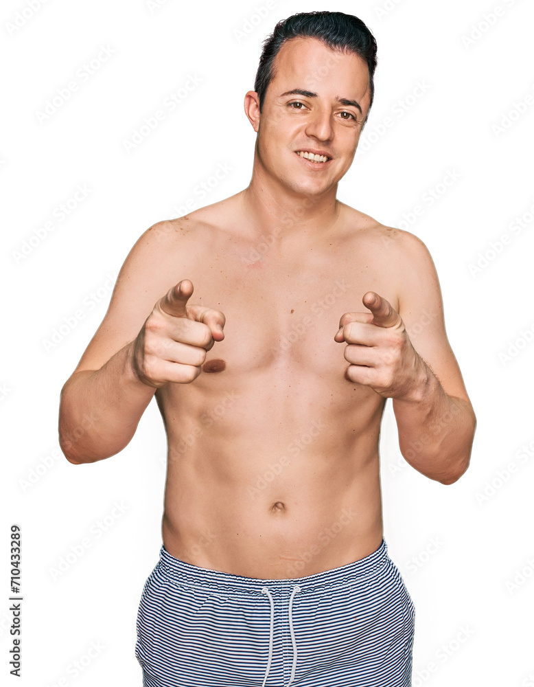 Fototapeta premium Handsome young man wearing swimwear shirtless pointing fingers to camera with happy and funny face. good energy and vibes.