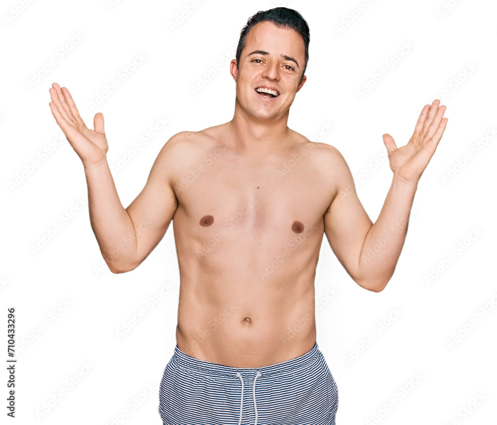 Fototapeta premium Handsome young man wearing swimwear shirtless celebrating crazy and amazed for success with arms raised and open eyes screaming excited. winner concept