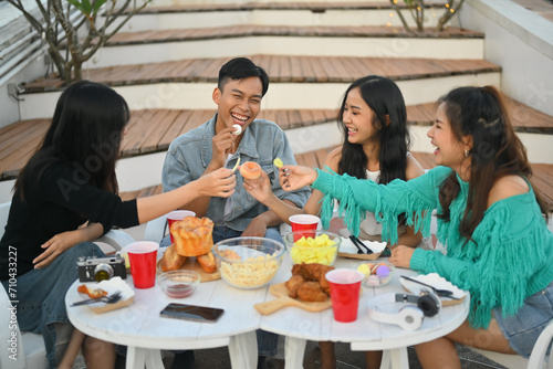 Group of cheerful friends having fun talking and drinking at party on rooftop.