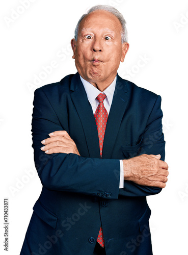 Senior business man with grey hair with arms crossed gesture making fish face with mouth and squinting eyes, crazy and comical. photo