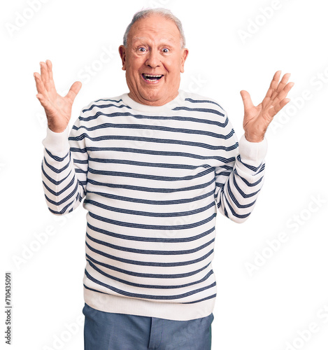 Senior handsome grey-haired man wearing casual striped sweater celebrating victory with happy smile and winner expression with raised hands