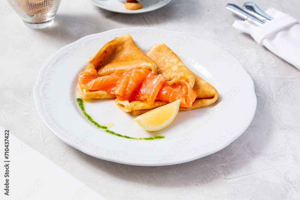 Pancakes with salmon and lemon on a white plate in a cafe, restaurant. Pancakes with salmon and lemon on a white plate in a cafe, restaurant.
