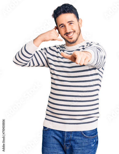 Young hispanic man wearing casual clothes smiling doing talking on the telephone gesture and pointing to you. call me.