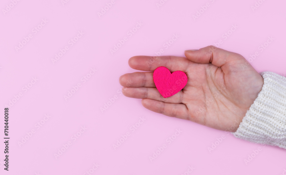 Fototapeta premium Woman's hands hold a pink heart on a pink background. Banner. Copy space. Top view. Selective focus.