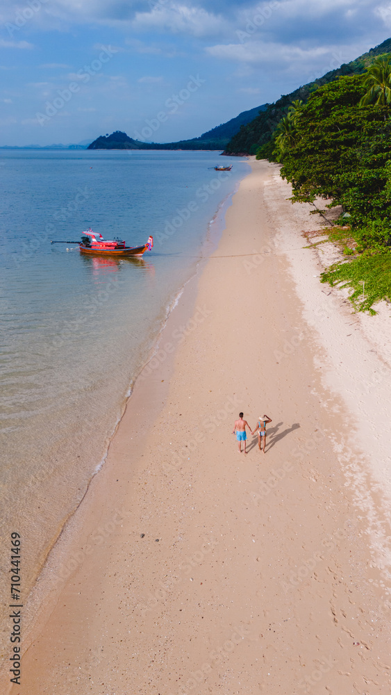 Fototapeta premium A beautiful view of a calm beach with crystal clear water on the blue sky at Koh Libong, Trang province, Thailand, Andaman Sea. A couple of men and woman walking on the beach