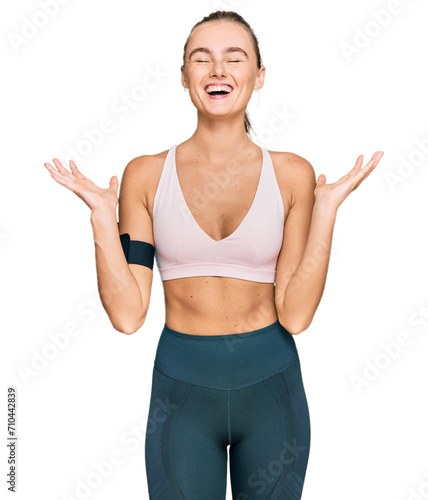 Beautiful young blonde woman wearing sportswear and arm band celebrating mad and crazy for success with arms raised and closed eyes screaming excited. winner concept © Krakenimages.com