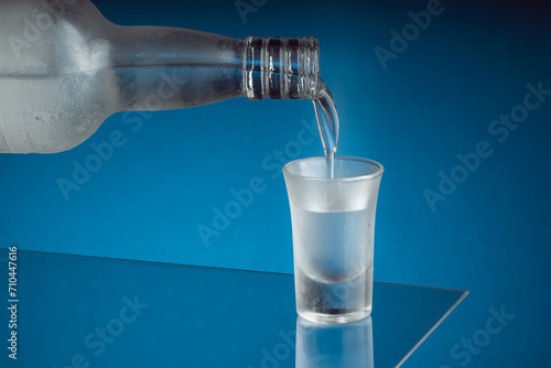 Billede på lærred Colorless alcohol being poured into a frosty shot glass standing on a glass plat