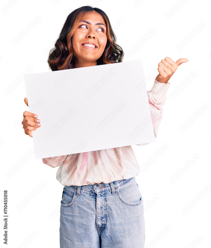 Young beautiful mixed race woman holding cardboard banner with blank space pointing thumb up to the side smiling happy with open mouth Young beautiful mixed race woman holding cardboard banner with blank space pointing thumb up to the side smiling happy with open mouth