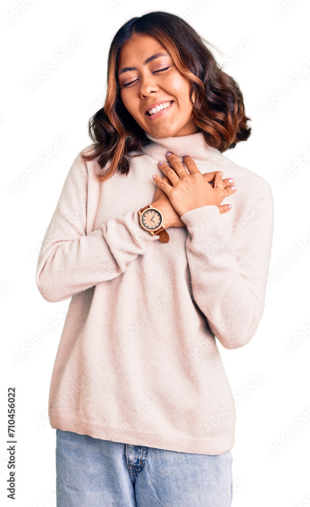 Young beautiful mixed race woman wearing winter turtleneck sweater smiling with hands on chest with closed eyes and grateful gesture on face. health concept. Young beautiful mixed race woman wearing winter turtleneck sweater smiling with hands on chest with closed eyes and grateful gesture on face. health concept.