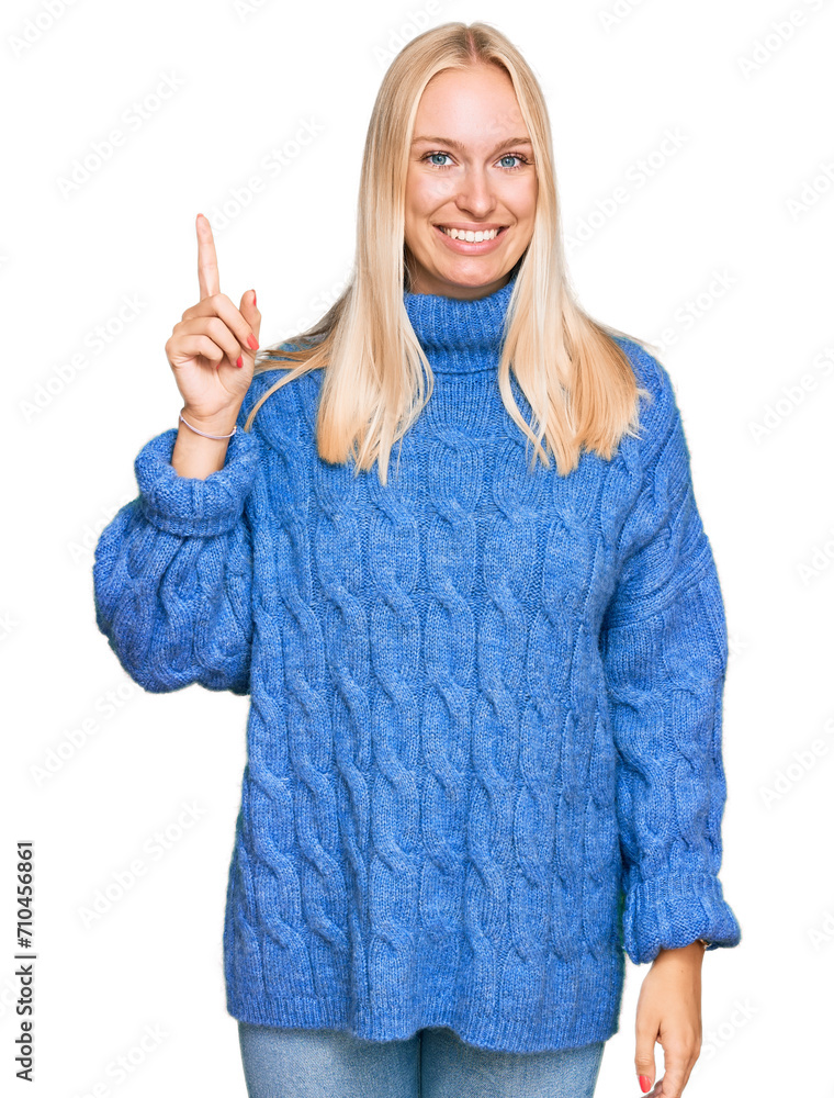 Young blonde girl wearing wool winter sweater pointing finger up with successful idea. exited and happy. number one. Young blonde girl wearing wool winter sweater pointing finger up with successful idea. exited and happy. number one.