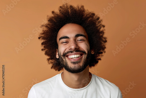Portrait of merry positive curly haired Hindu man smiles pleasantly being in good mood dressed in casual t shirt looks directly at camera isolated over brown background © Nate