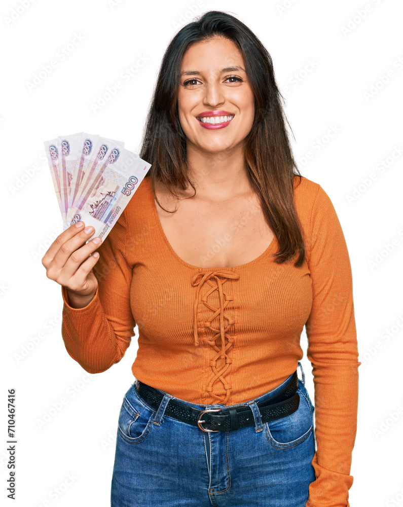 Beautiful hispanic woman holding russian 500 ruble banknotes looking positive and happy standing and smiling with a confident smile showing teeth Beautiful hispanic woman holding russian 500 ruble banknotes looking positive and happy standing and smiling with a confident smile showing teeth
