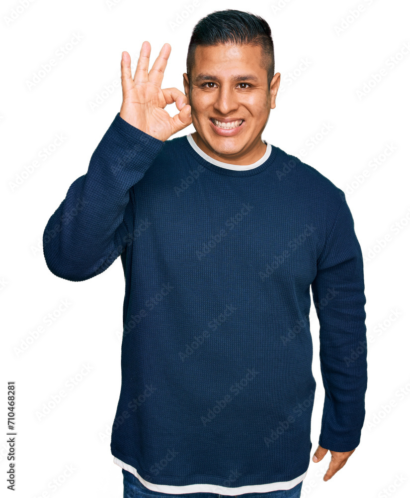 Naklejka premium Young latin man wearing casual clothes smiling positive doing ok sign with hand and fingers. successful expression.