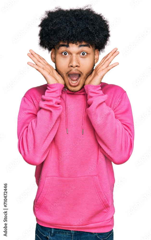 Young african american man with afro hair wearing casual pink sweatshirt afraid and shocked, surprise and amazed expression with hands on face Young african american man with afro hair wearing casual pink sweatshirt afraid and shocked, surprise and amazed expression with hands on face