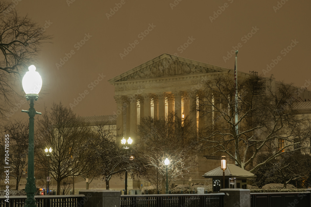 Obraz premium Supreme Court of the United States in winter. Night photo of Supreme Court of the United States in Washington DC in snow. SCOTUS building in snow. Winter Capitol hill, Washington DC.