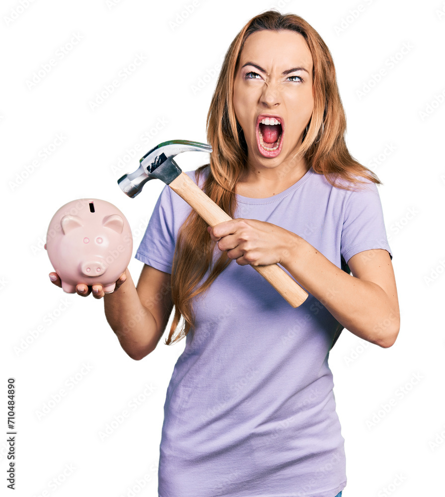 Φωτογραφία Young caucasian woman holding piggy bank and hammer angry and mad screaming frustrated and furious, shouting with anger looking up