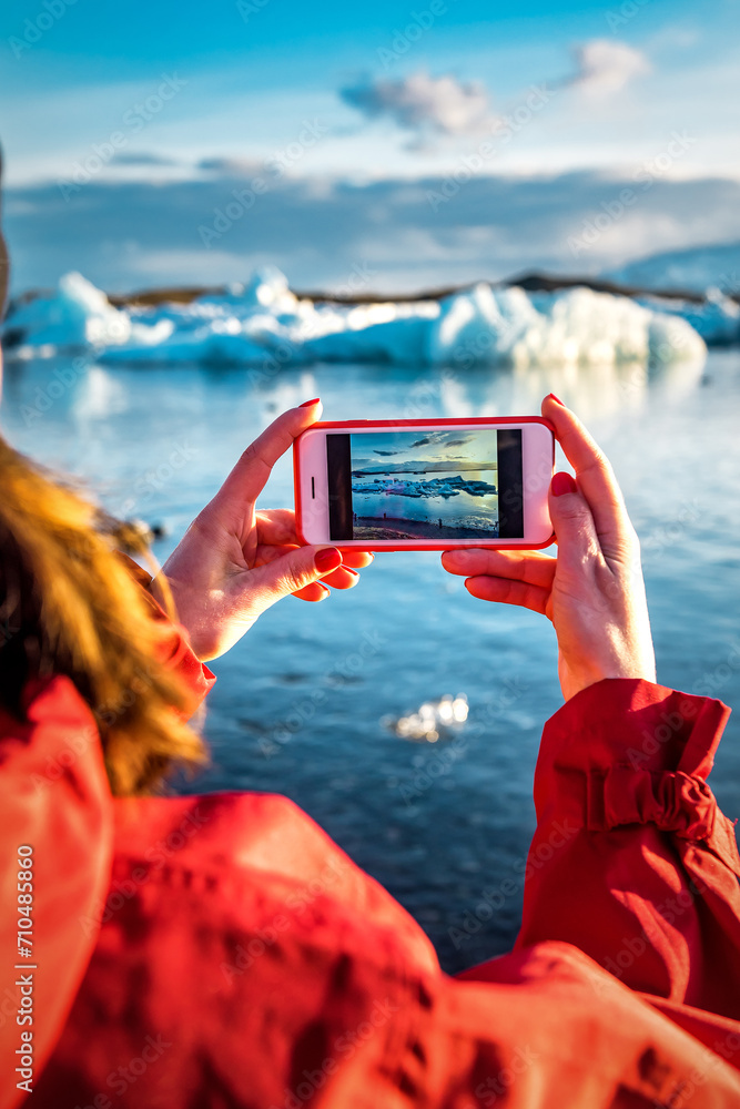 Woman taking a picture by smartphone of a blue iceberg in ice lagoon at Iceland. Woman taking photograph of beautiful Icelandic nature in Vatnajokull.