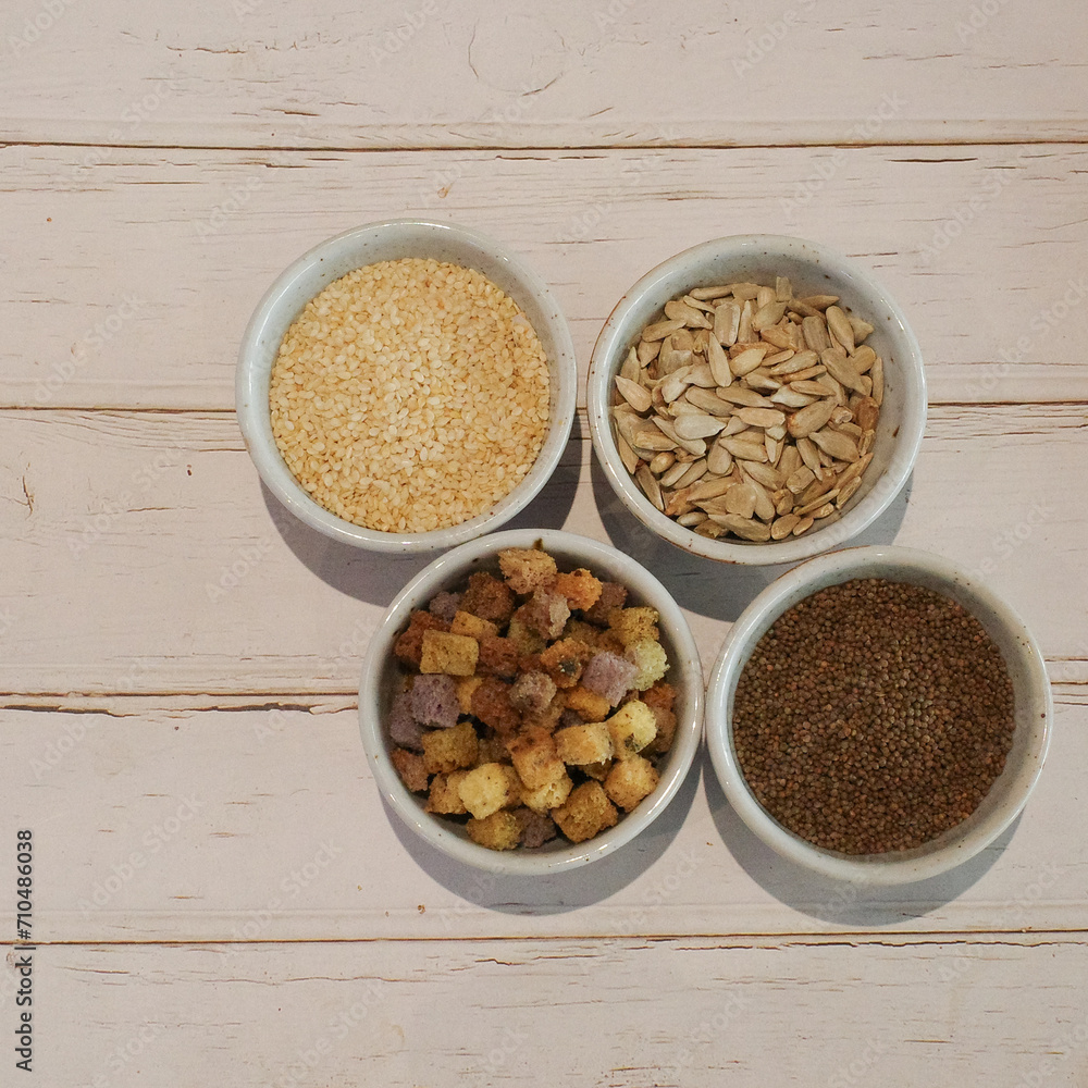 Grain seeds (white sesame, sunflower seed, chia seed and whole wheat dried bread) in four small white cups. Grain seeds (white sesame, sunflower seed, chia seed and whole wheat dried bread) in four small white cups.