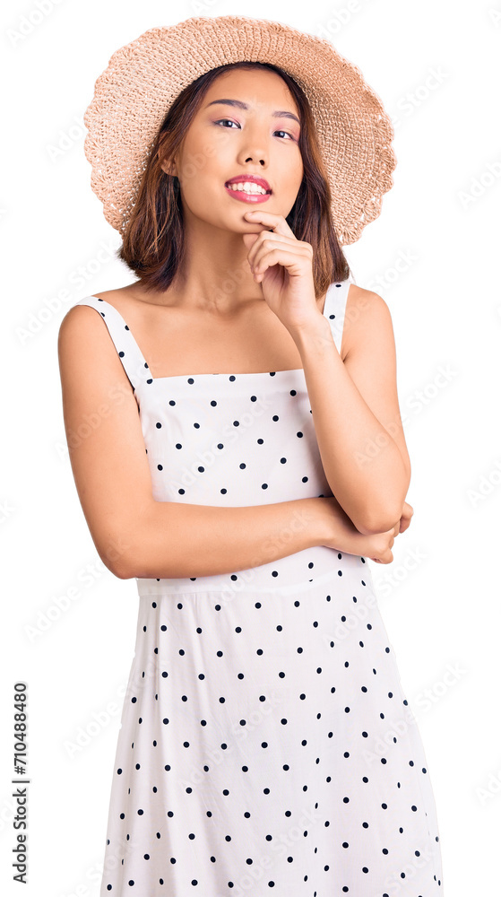 Young beautiful chinese girl wearing summer hat looking confident at the camera with smile with crossed arms and hand raised on chin. thinking positive. Young beautiful chinese girl wearing summer hat looking confident at the camera with smile with crossed arms and hand raised on chin. thinking positive.