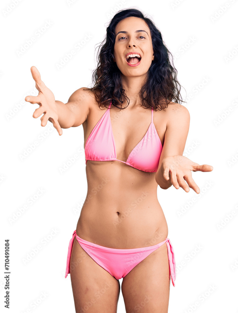 Young beautiful hispanic woman wearing bikini smiling cheerful offering hands giving assistance and acceptance. Young beautiful hispanic woman wearing bikini smiling cheerful offering hands giving assistance and acceptance.