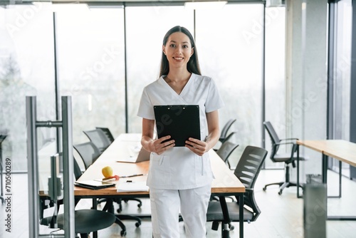 Black notepad in hands. Female doctor in white coat is indoors