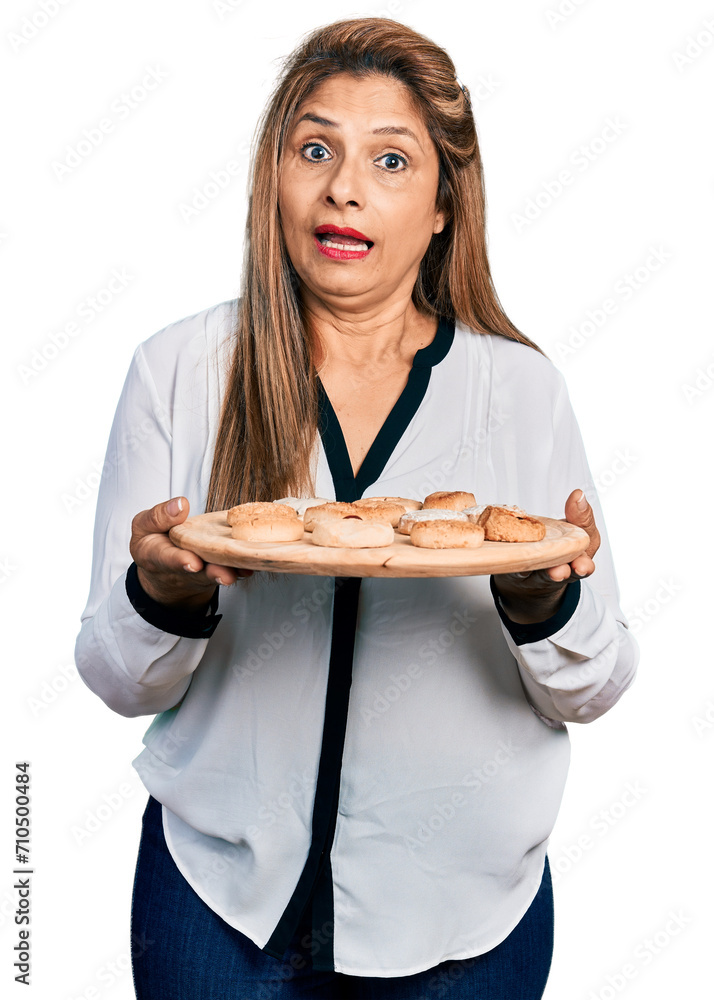 Middle age latin woman eating pastries clueless and confused expression. doubt concept. Middle age latin woman eating pastries clueless and confused expression. doubt concept.