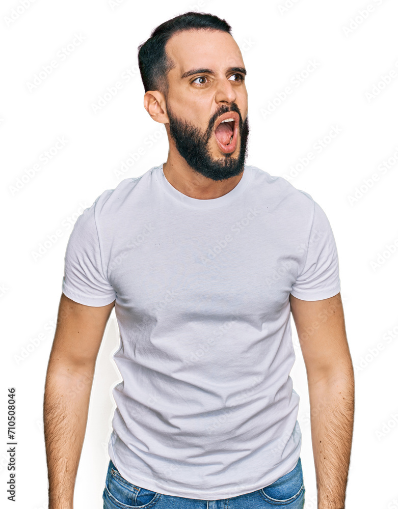 Young man with beard wearing casual white t shirt angry and mad screaming frustrated and furious, shouting with anger. rage and aggressive concept. Young man with beard wearing casual white t shirt angry and mad screaming frustrated and furious, shouting with anger. rage and aggressive concept.