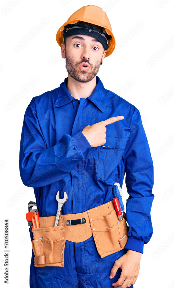 Young hispanic man wearing worker uniform surprised pointing with finger to the side, open mouth amazed expression. Young hispanic man wearing worker uniform surprised pointing with finger to the side, open mouth amazed expression.