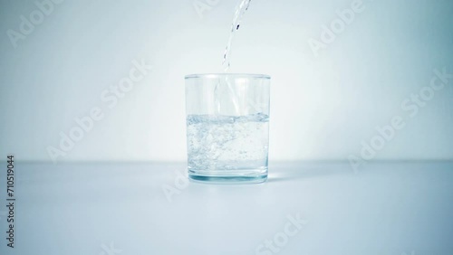 Water is Poured into a Transparent Glass. Liquid is poured into a Glass on a white background. The glass is filled with Clean Water. Slow motion.