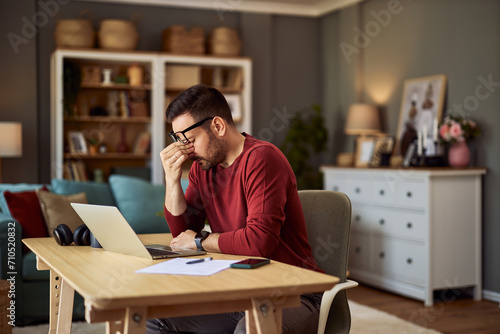 A tired freelance man sitting at a desk in front of a laptop and pinching his nose. photo