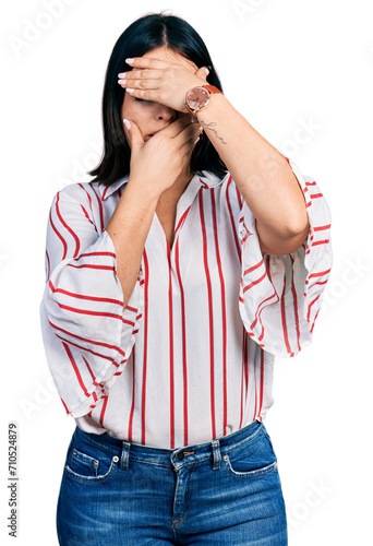 Young hispanic girl wearing casual clothes covering eyes and mouth with hands, surprised and shocked. hiding emotion