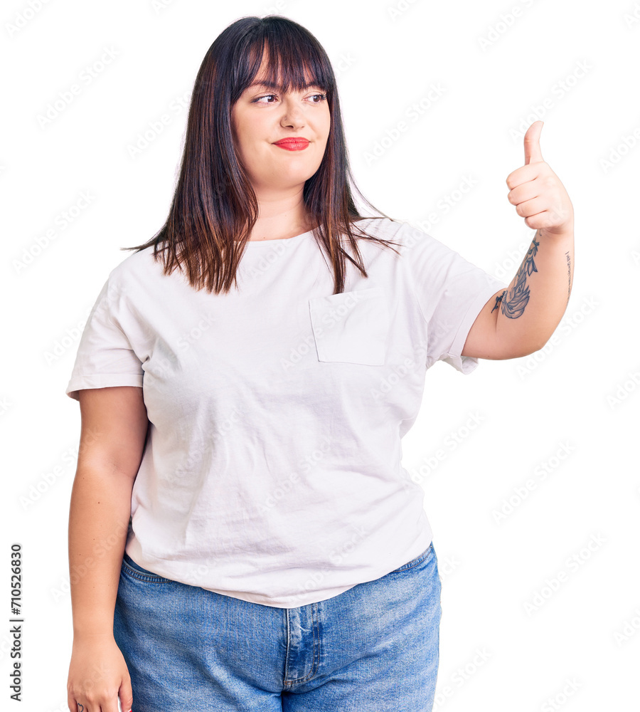 Young plus size woman wearing casual clothes looking proud, smiling doing thumbs up gesture to the side Young plus size woman wearing casual clothes looking proud, smiling doing thumbs up gesture to the side