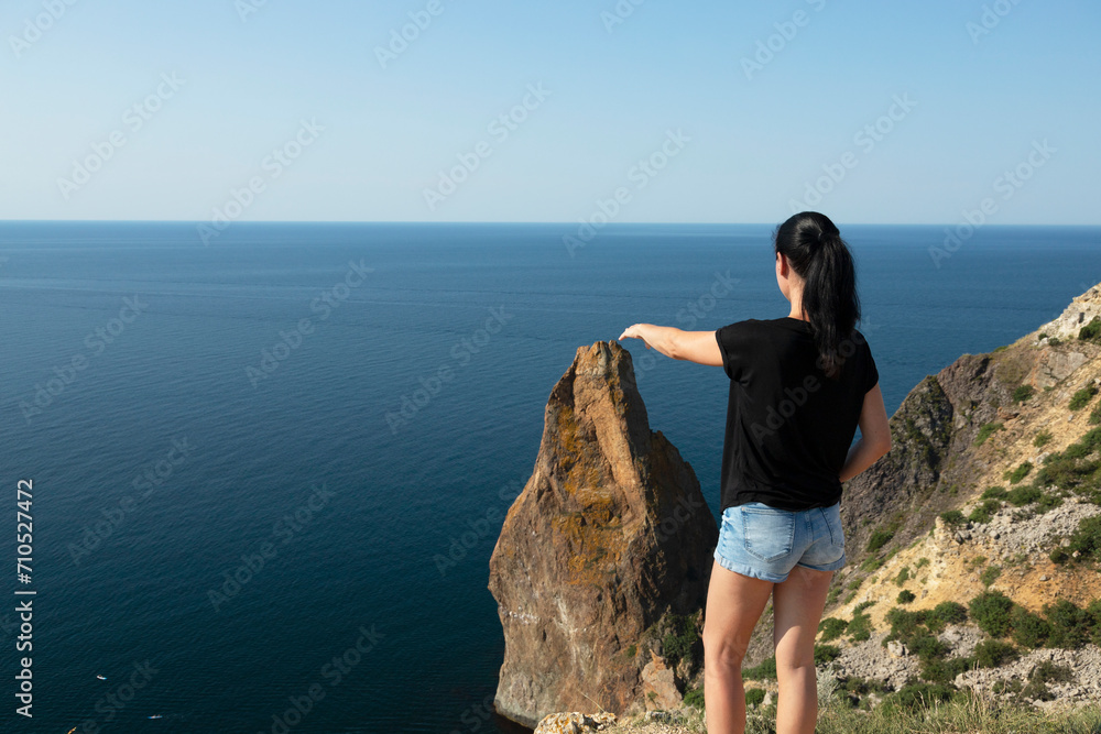 A beautiful woman with dark hair on the edge of a mountain against the backdrop of the sea and sky. Spread your arms in preparation for the jump and flight.