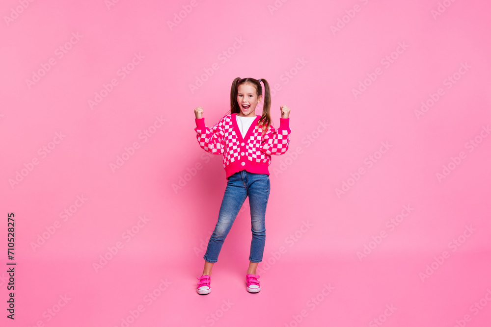 Full size photo of satisfied girl with tails dressed knit cardigan clenching fists celebrate winning isolated on pink color background Full size photo of satisfied girl with tails dressed knit cardigan clenching fists celebrate winning isolated on pink color background