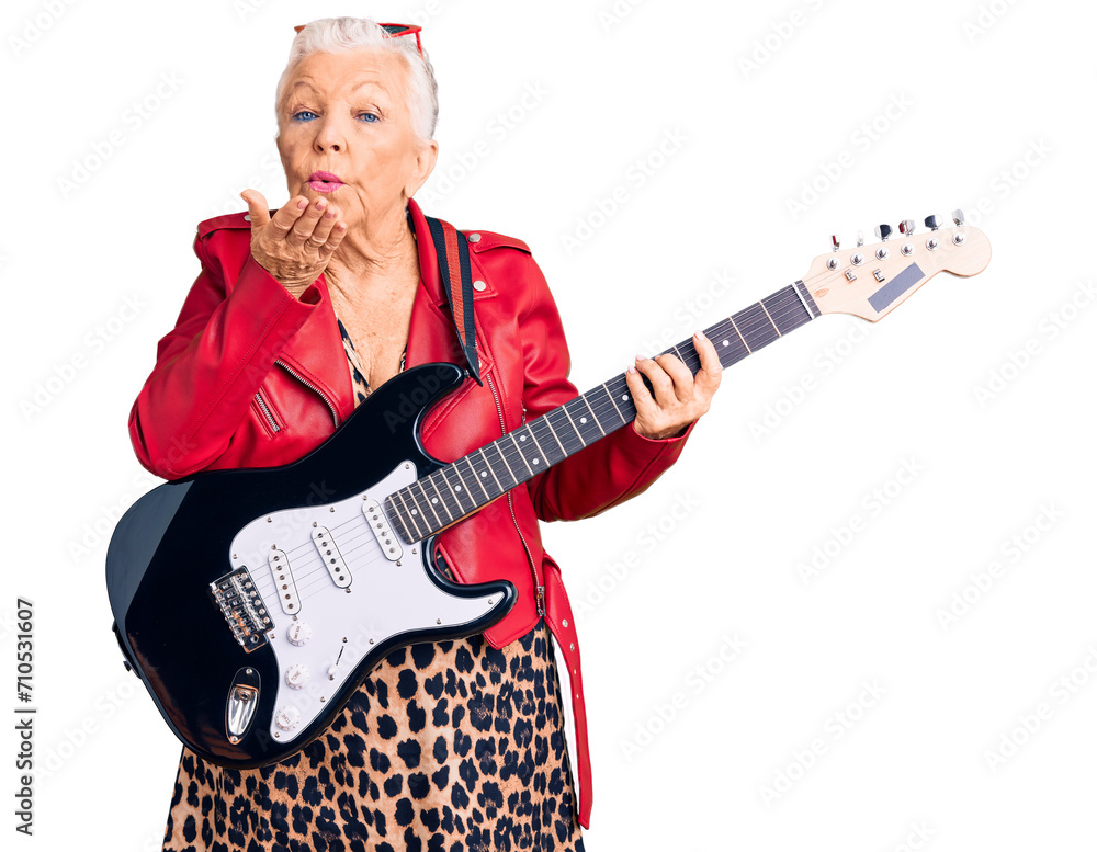 Senior beautiful woman with blue eyes and grey hair wearing a modern look playing electric guitar looking at the camera blowing a kiss with hand on air being lovely and sexy. love expression.
