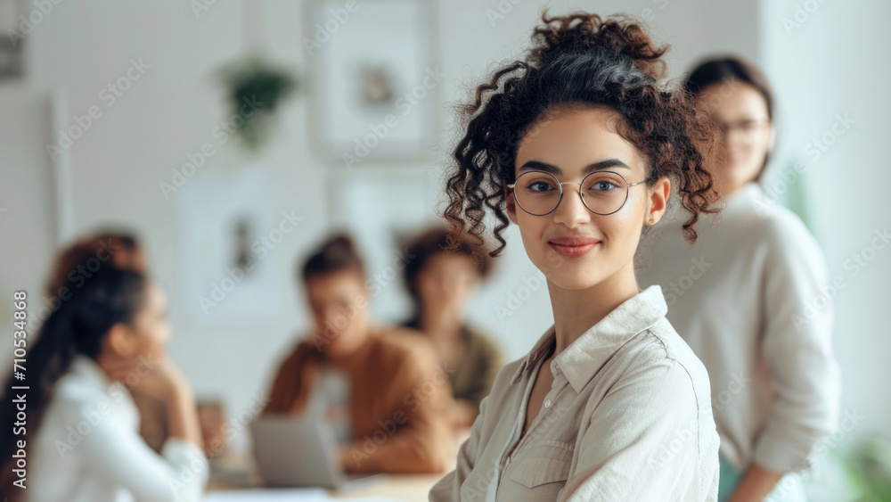 An upbeat young woman in business attire, holding glasses, radiating confidence, and a friendly smile. She could be leading a meeting or workshop