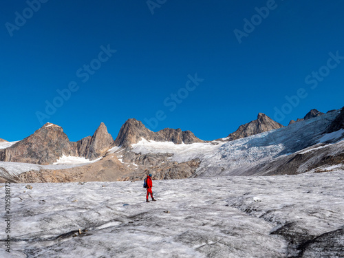 A man in red clothes stands on a glacier in front of the Niialiqaq mountain range in Greenland.
