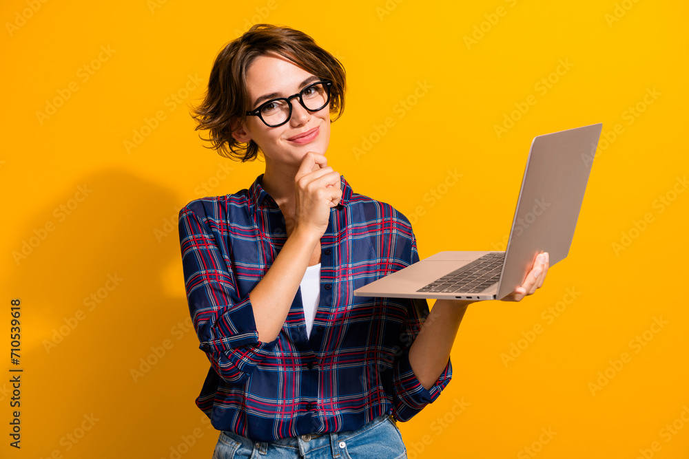 Photo of minded intelligent woman dressed plaid shirt in eyewear holding laptop think business isolated on yellow color background Photo of minded intelligent woman dressed plaid shirt in eyewear holding laptop think business isolated on yellow color background