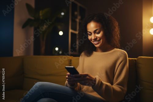 Mulher sentada no sofá em sua casa de noite usando o celular 