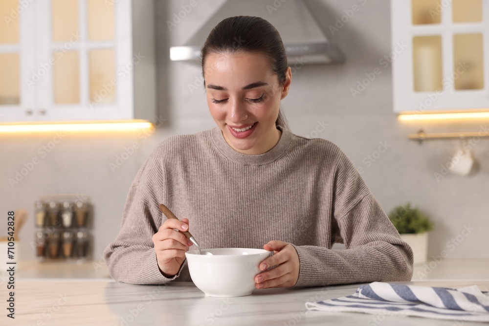 Smiling woman eating tasty soup at white marble table in kitchen Smiling woman eating tasty soup at white marble table in kitchen