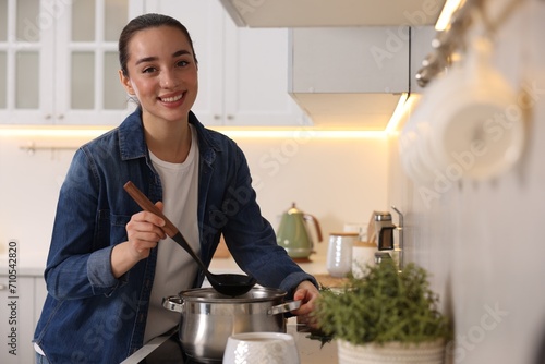 Smiling woman with ladle cooking soup in kitchen photo