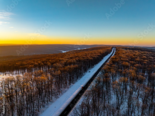 aerial view of the treetops of the forest and a road illuminated by the setting sun during winter in moldova