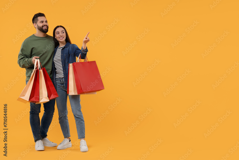 Happy couple with shopping bags looking at something on orange background. Space for text Happy couple with shopping bags looking at something on orange background. Space for text