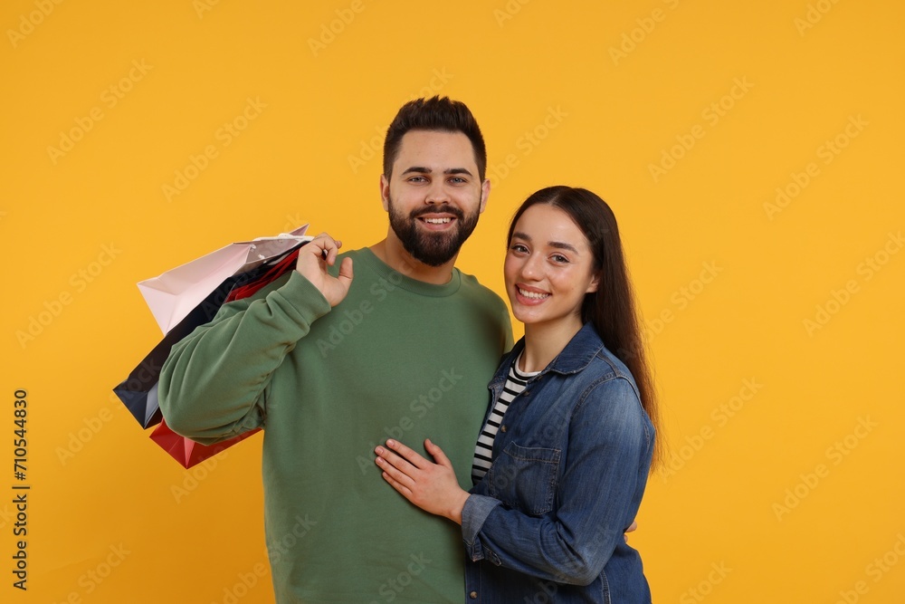 Fototapeta premium Happy couple with shopping bags on orange background